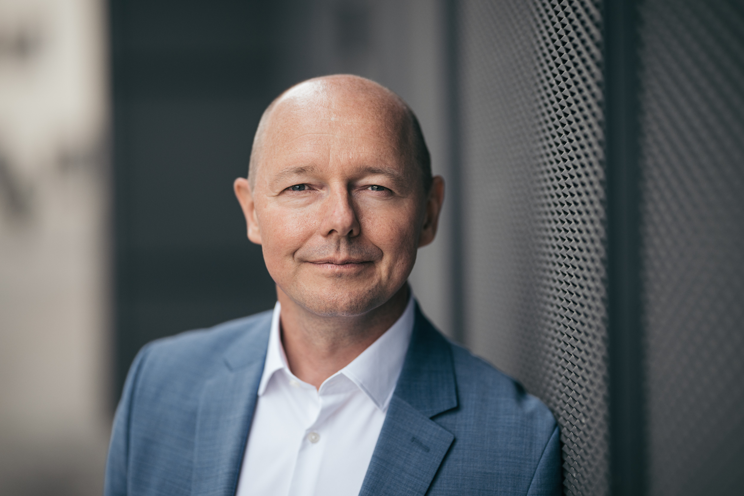 Close-up portrait of Jan Buschmeyer beside an architectural metal screen